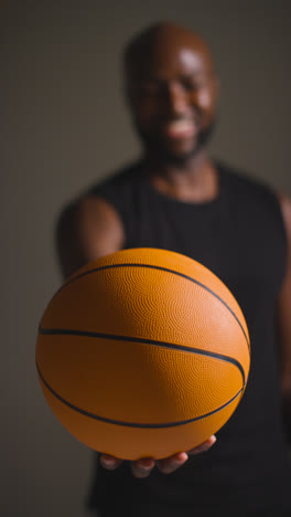 Vertikales-Videostudio-Vertikale-Videoporträtaufnahme-Eines-Lächelnden-Männlichen-Basketballspielers,-Der-Den-Ball-In-Richtung-Kamera-Hält